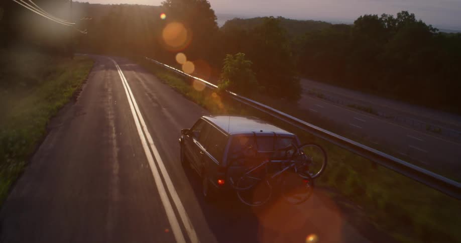 A car drives on a rural road at sunset
