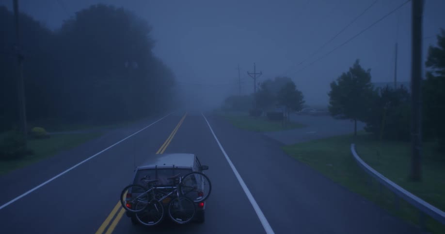A car drives down the road into the fog