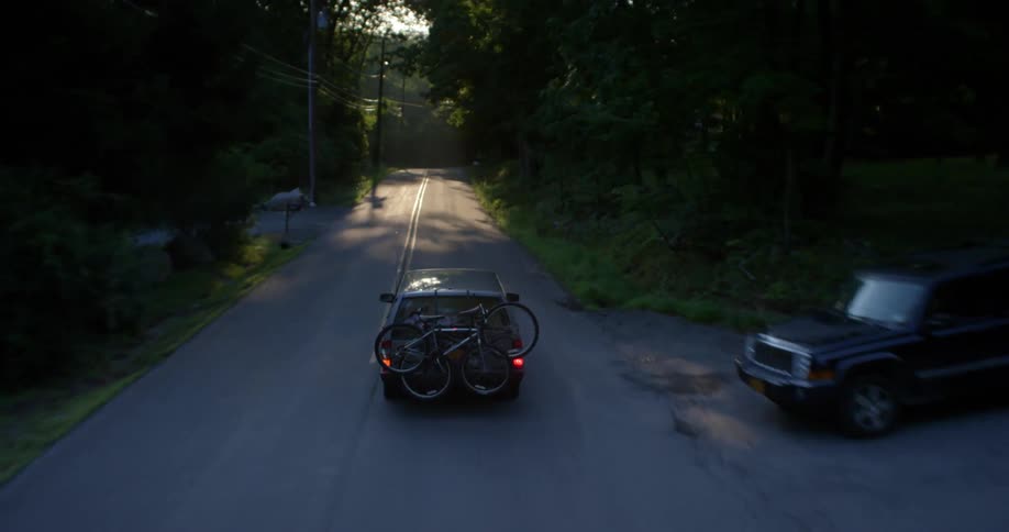 Vehicle driving down a country road carrying bicycles on its rear near sunset