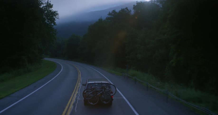An suv carrying bicycles drives along a rural road