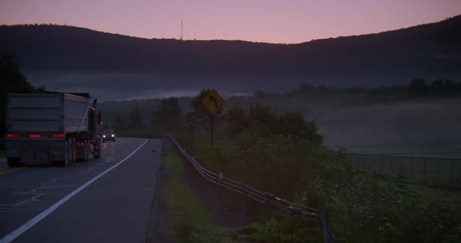 Truck driving down a country road at sunrise
