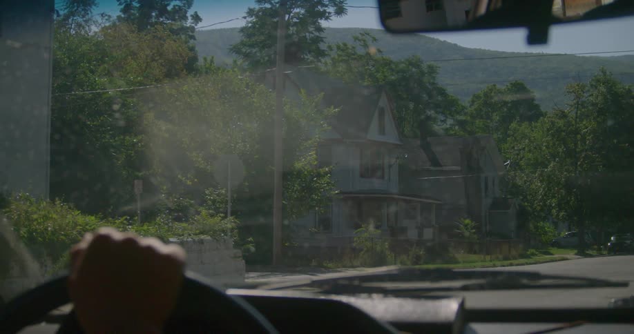 A person drives down a road lined with houses and trees