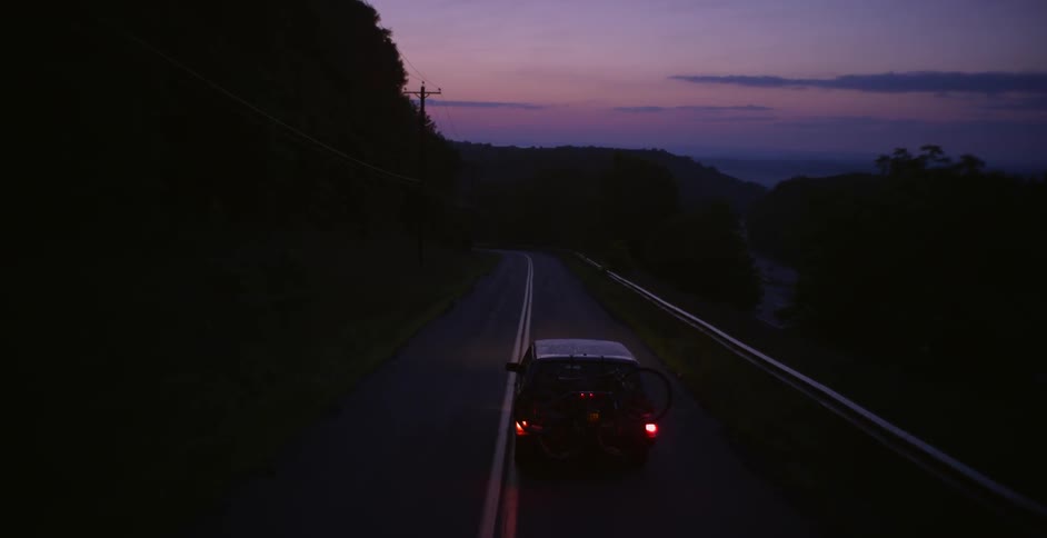 An suv carrying bicycles drives along a rural road
