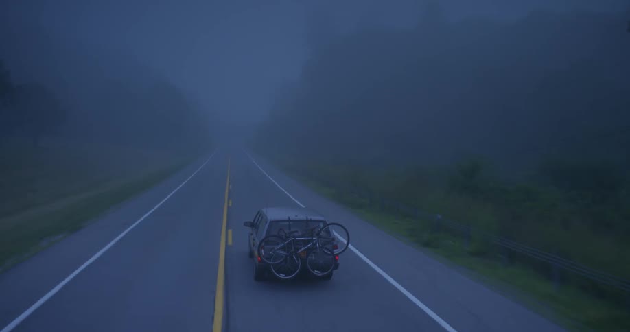 An suv with bikes on the back drives down a foggy road