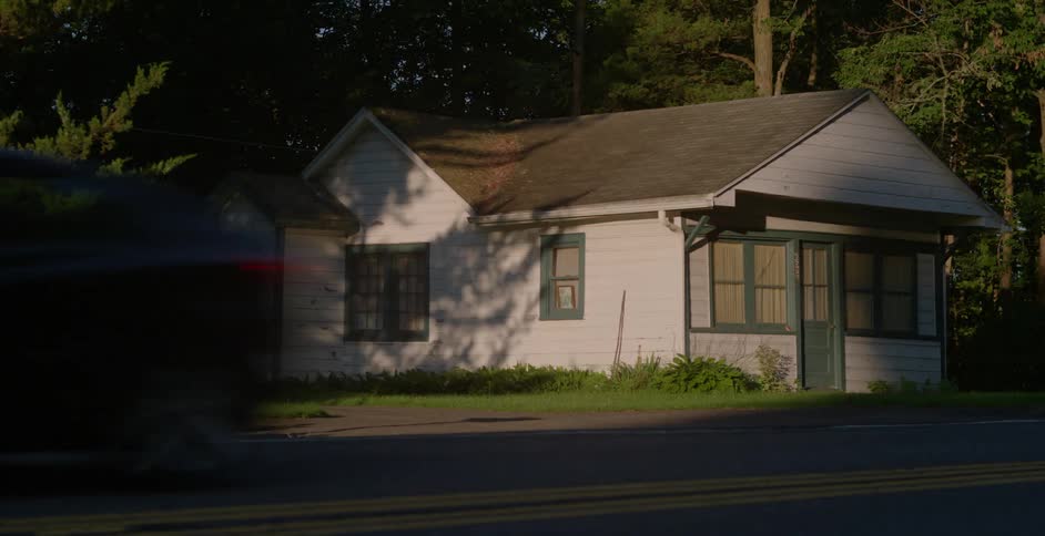 Cars drive past a small house