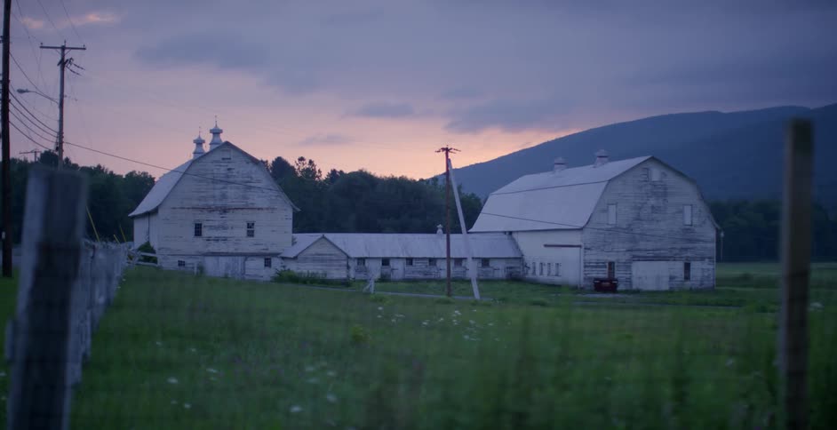 A large farm barn is on the grass at dawn
