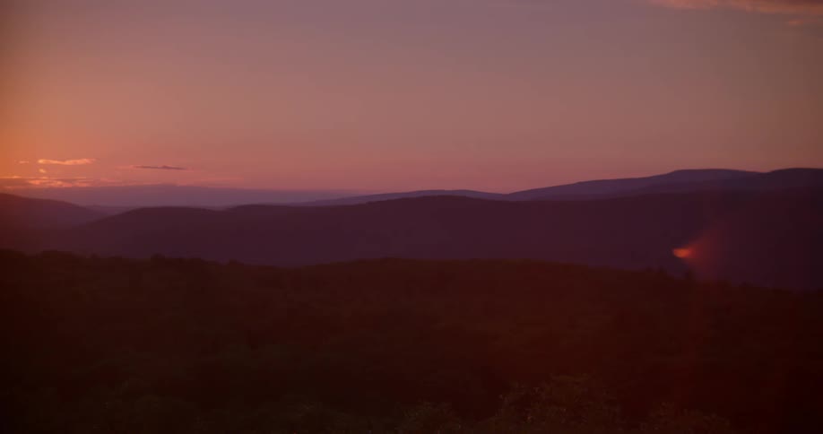 The sun is setting beyond rolling hills