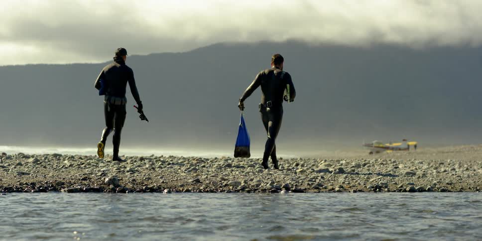 Divers walk with their gear on a rocky beach