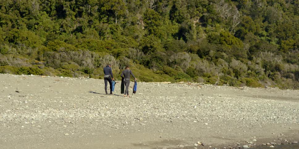 Two men carrying snorkeling gear walk across a beach