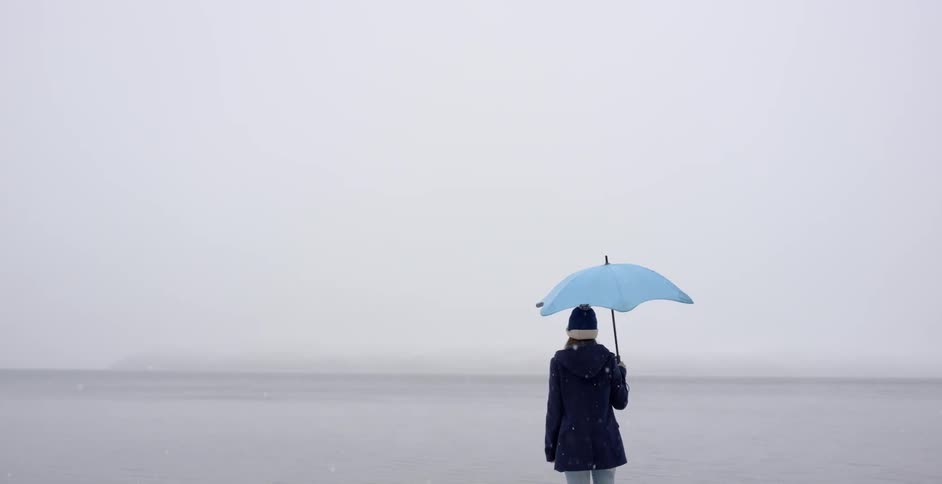 Snow falls on a woman holding an umbrella