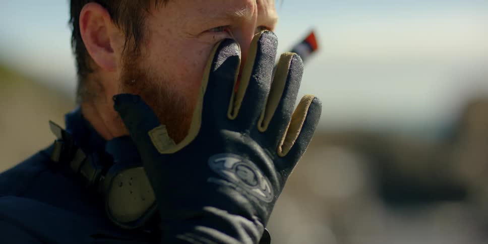 A man wearing scuba gear looks around and rubs beneath his eye