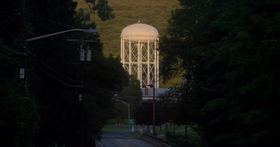 Cars drive on a street with a water tower in the distance