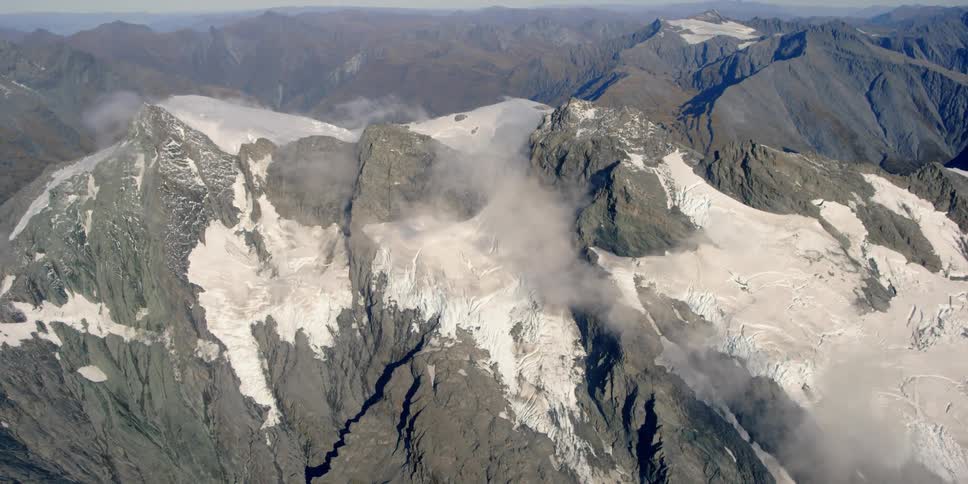 Wispy clouds move over snow-covered mountain peaks during the day