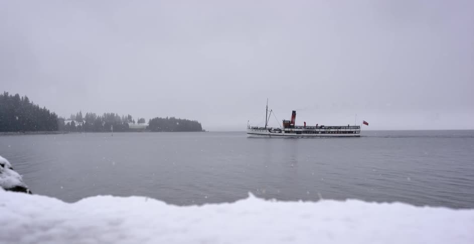 A large ship sails in the water as it snows