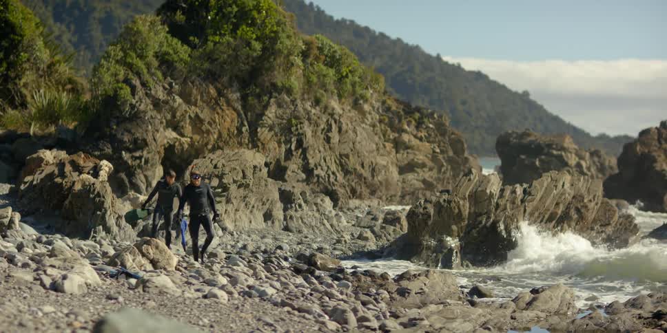 Two men wearing snorkeling gear walk across a beach