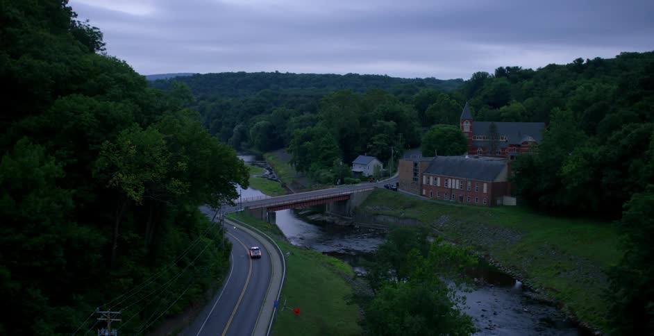 A car drives down the road by the creek
