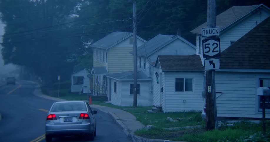 Vehicles drive down a road surrounded by houses