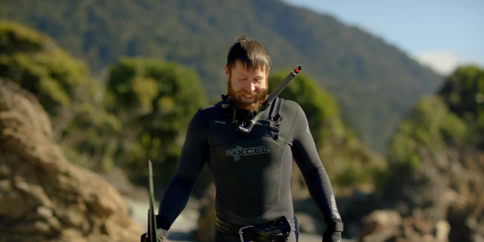 A man wearing a wetsuit and snorkeling gear walks on the beach