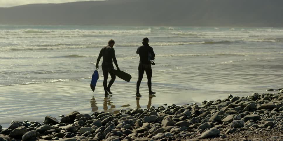Two people walk along the water by the beach