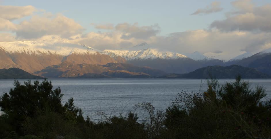 Clouds hover above a mountain range and a lake during the day