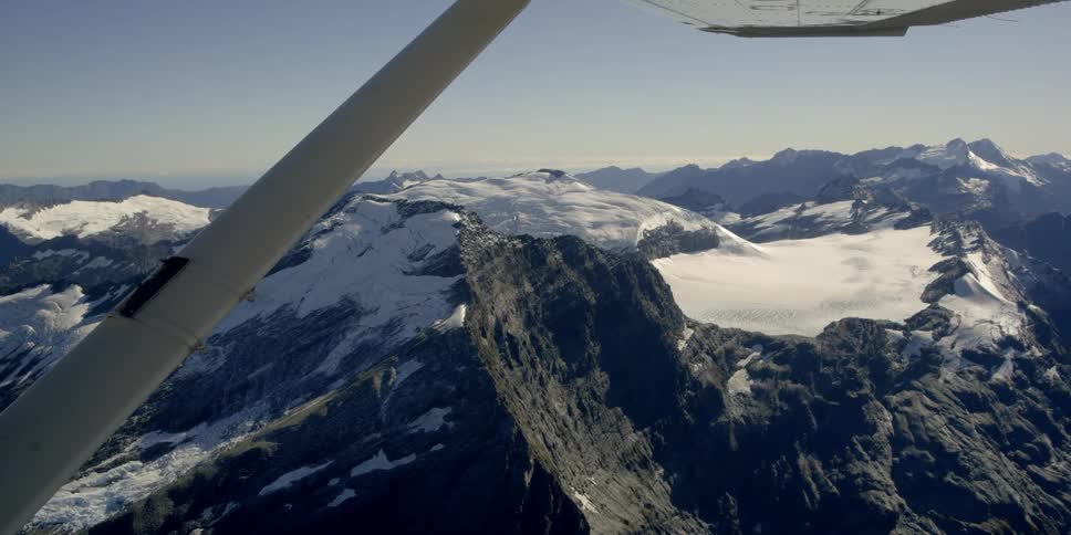 The wing of a small plane as it flies over mountains