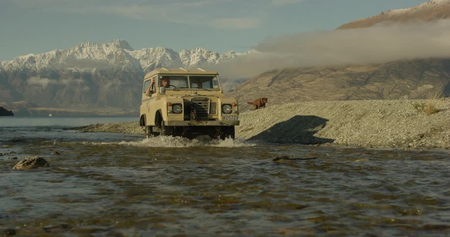 A jeep drives down the bank and up a shallow stream