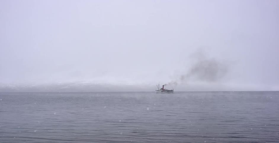 A ship on the ocean under a gray sky and snowfall