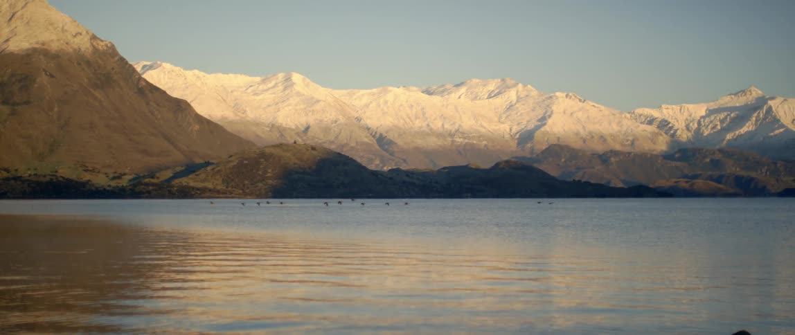 Birds fly low over a lake near mountains
