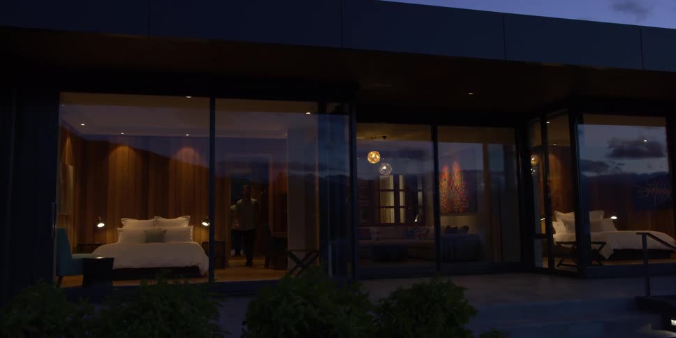 A man walks in a bedroom with floor to ceiling windows