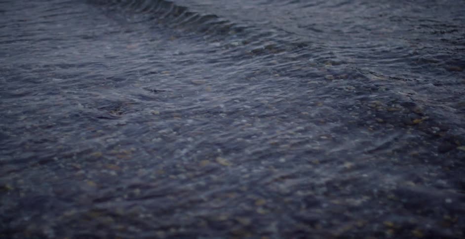 Pebbles underneath water flowing to shore