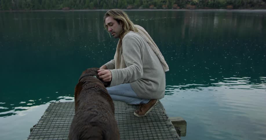 A man pets his dog on the pier