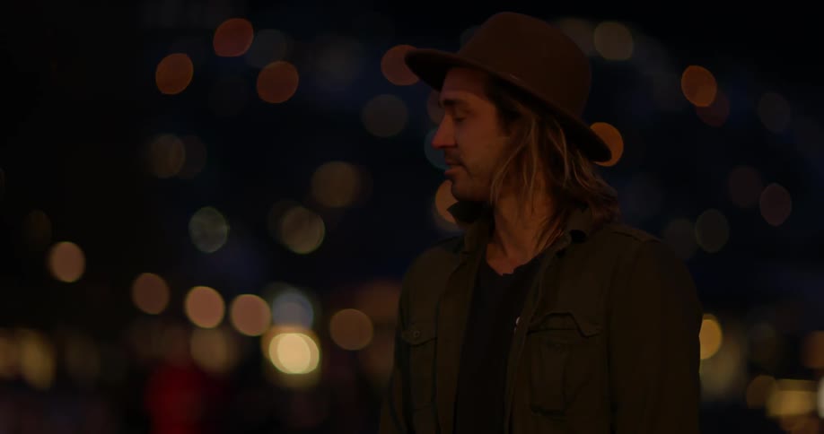 A man stands outside at night with city lights in the background