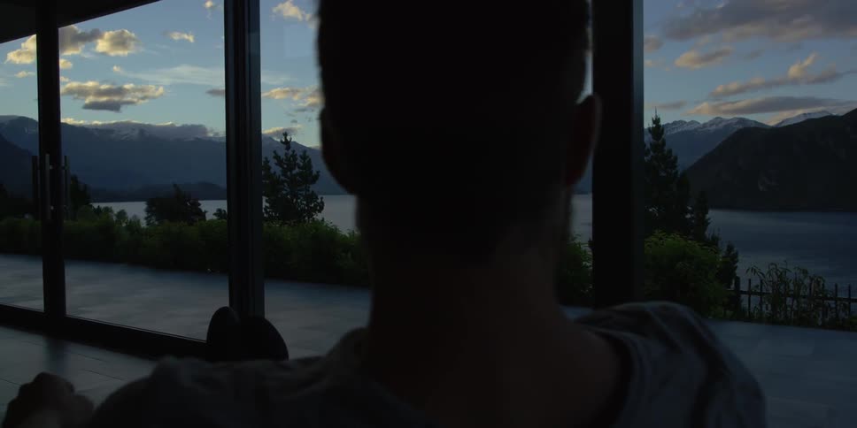 A man looks out a window towards a mountain lake