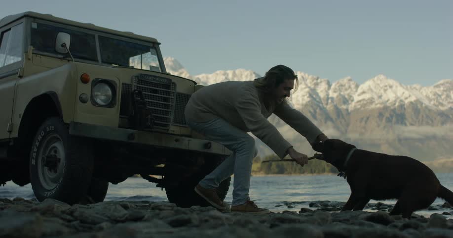A man plays with his dog on a lakeshore