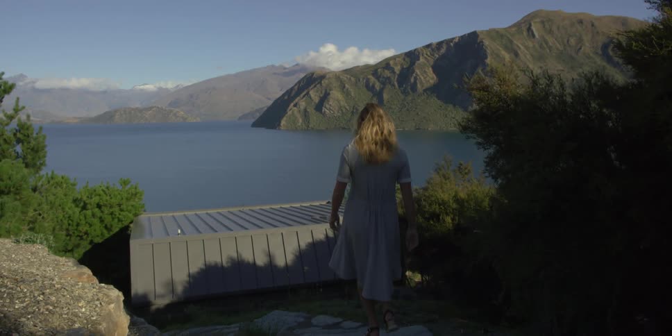 A woman walks towards a mountain lake