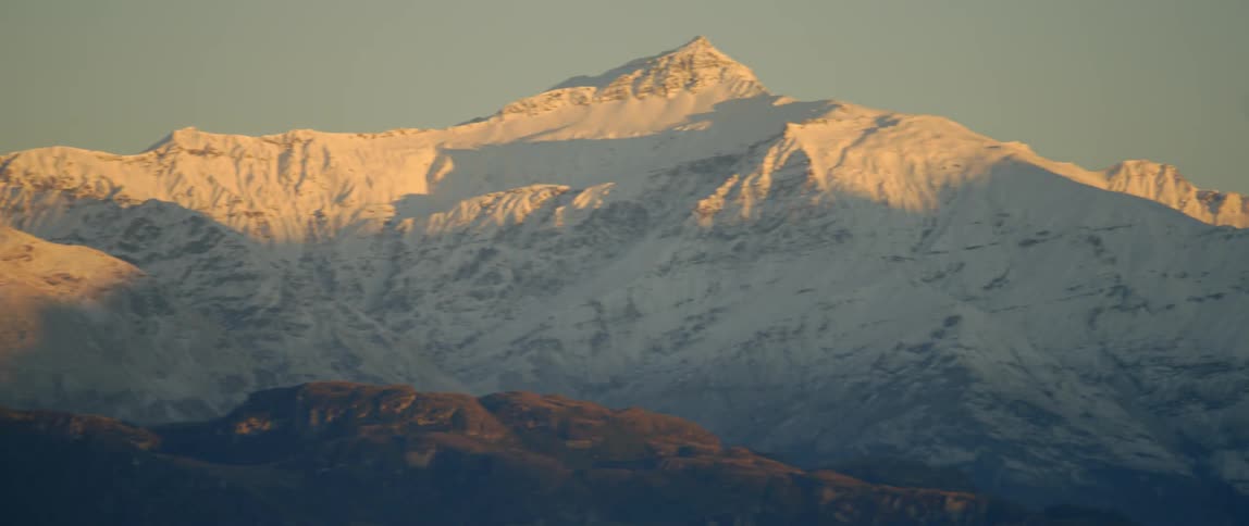 The sun illuminates a snow-covered mountain range at dawn