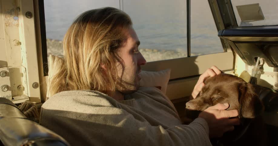 A man sits with his dog in a vehicle and rubs its head