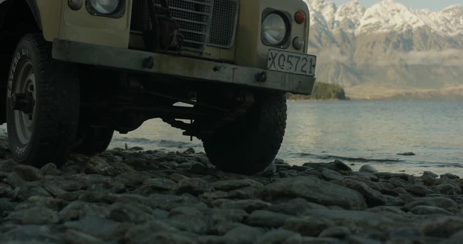 A jeep drives on the rocks by the water
