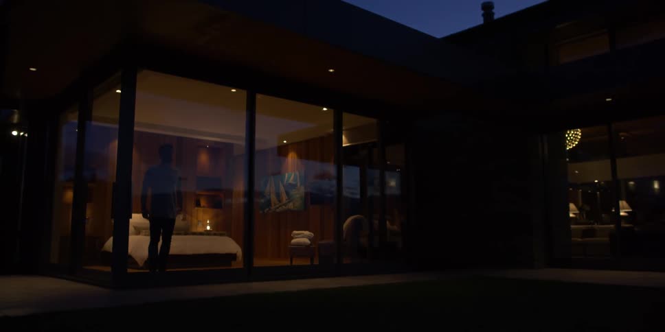 A man stands in a bedroom looking out the floor to ceiling window