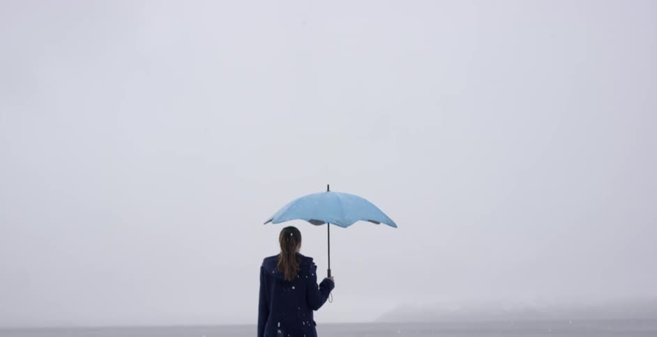 A woman holds an umbrella as she stands in a snow-covered landscape