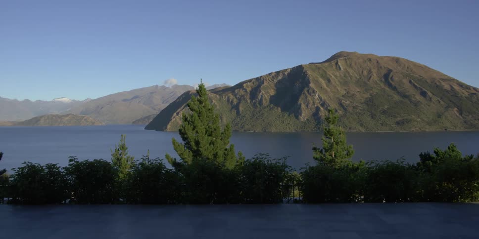 A man opens a sliding glass door overlooking a mountain lake