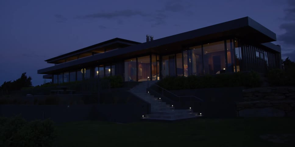 A house with floor to ceiling windows is shown at night