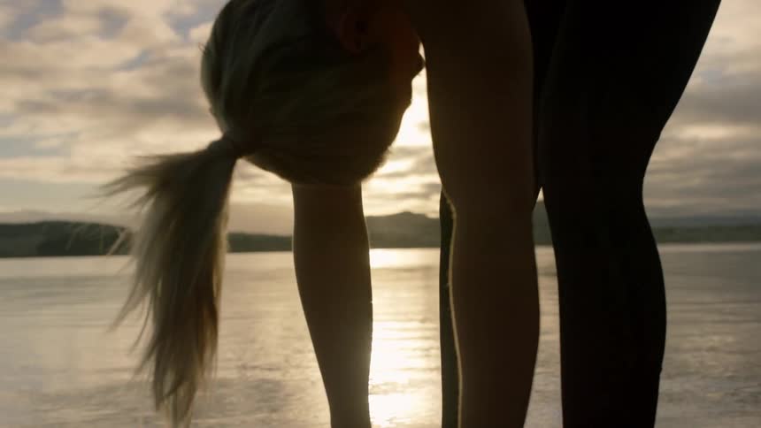 A woman leans forward stretching by the water