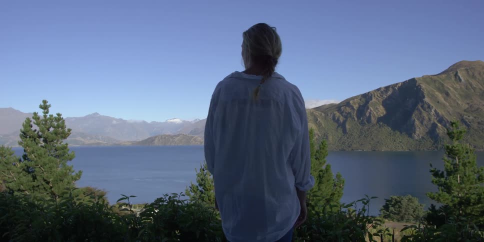 A woman stands looking over a view of a lake