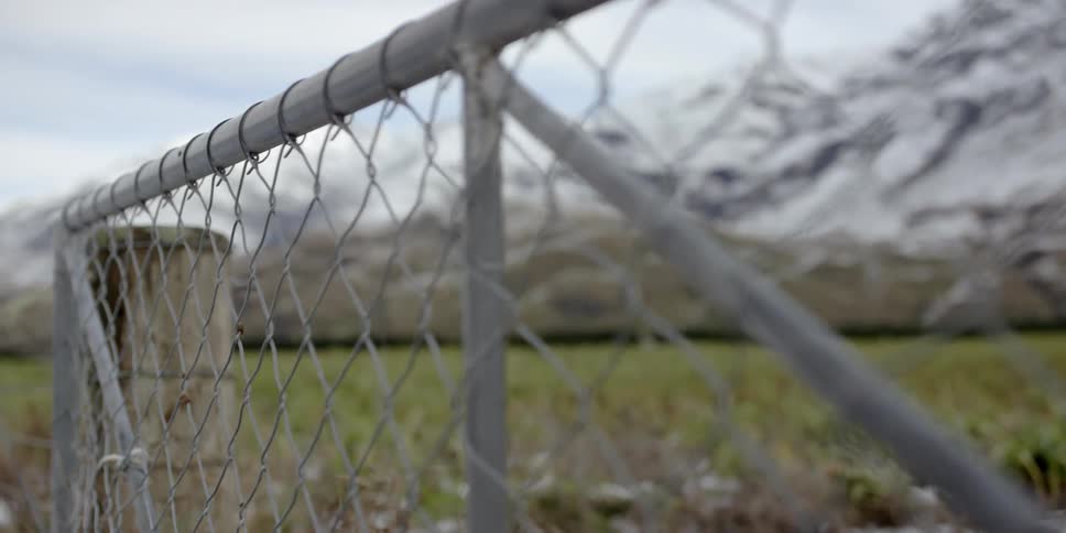 A snowy mountain is seen through a chainlink fence