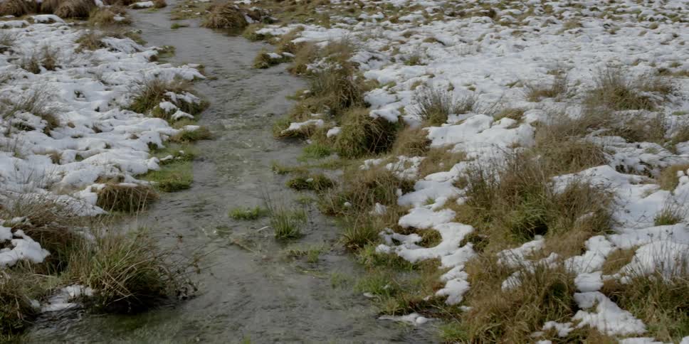 Stream flowing through snow covered plains near a large mountain
