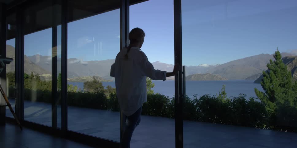 A man opens a sliding glass door that overlooks a mountain lake