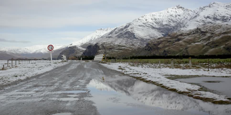 A puddle covers a muddy road surrounded by snowy mountains