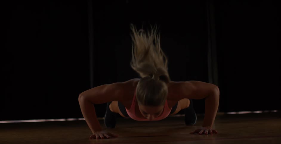 Woman does pushups in a dim room