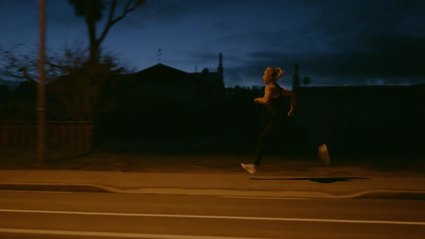 A woman jogs on a sidewalk at night